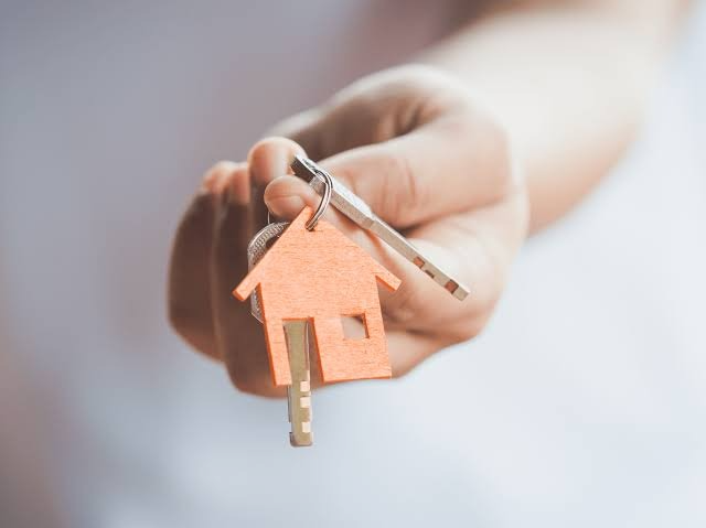 Hand holding a house-shaped keychain and key, representing buying landed property in Singapore
